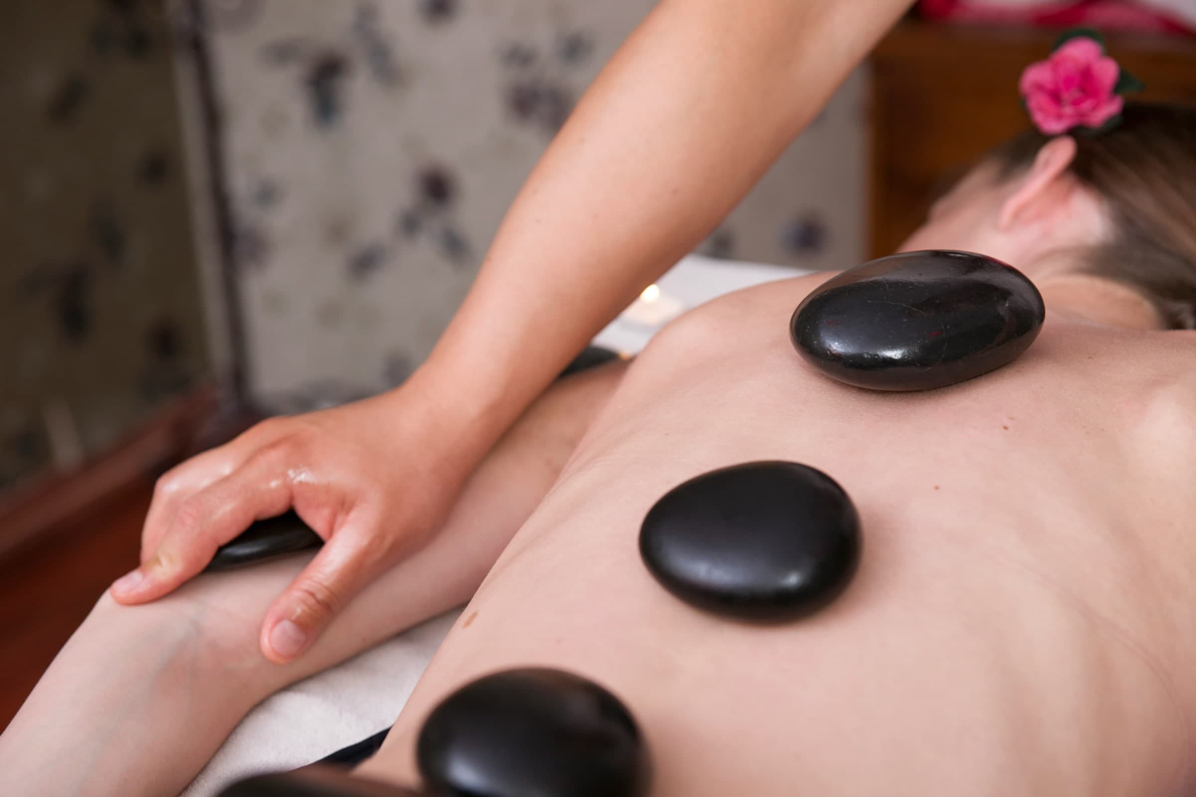 Registered massage therapist applying heated black stone to client's back during hot stone massage therapy